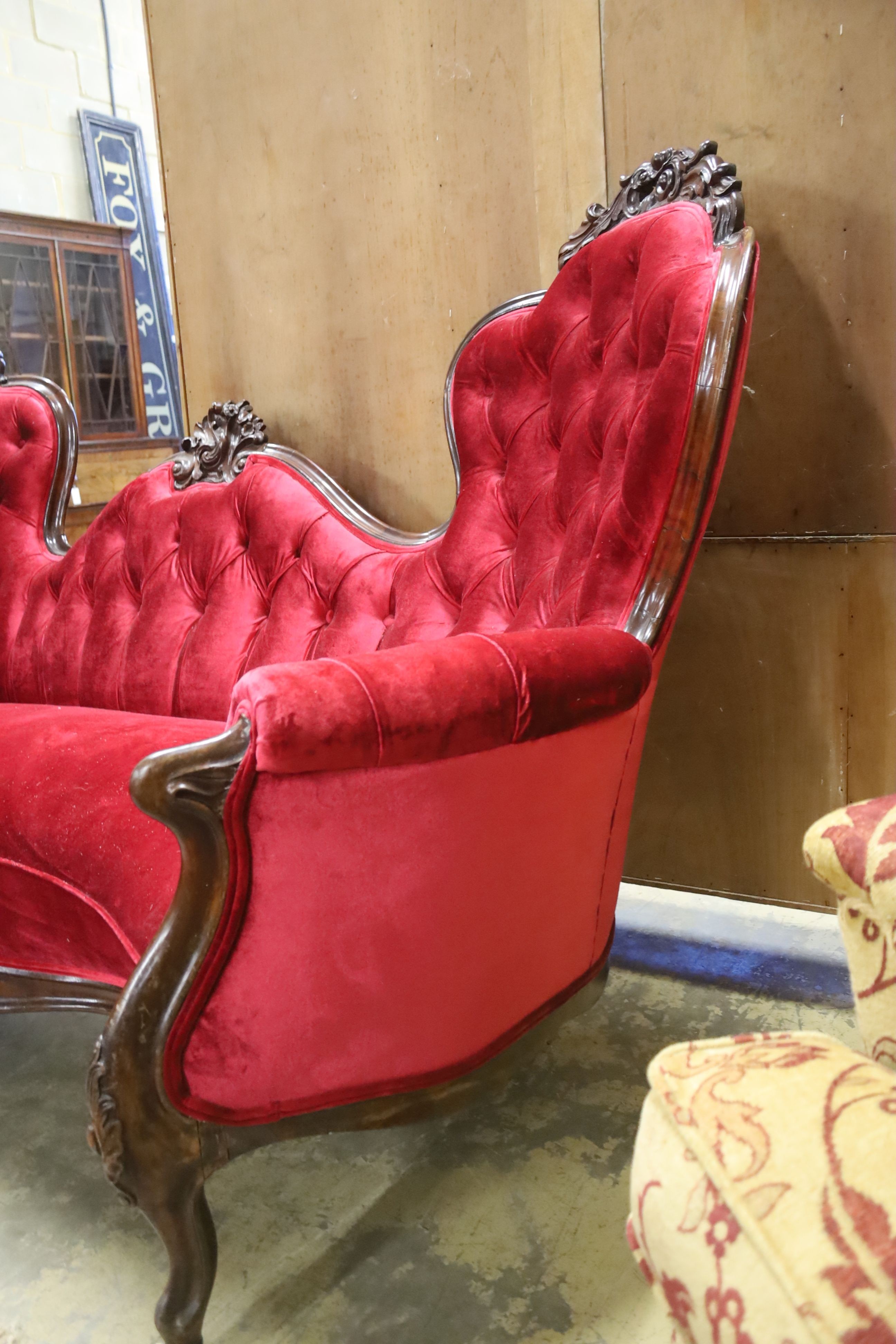 A Victorian carved rosewood double spoon back settee upholstered in deep buttoned scarlet velvet, length 200cm, depth 96cm, height 122cm